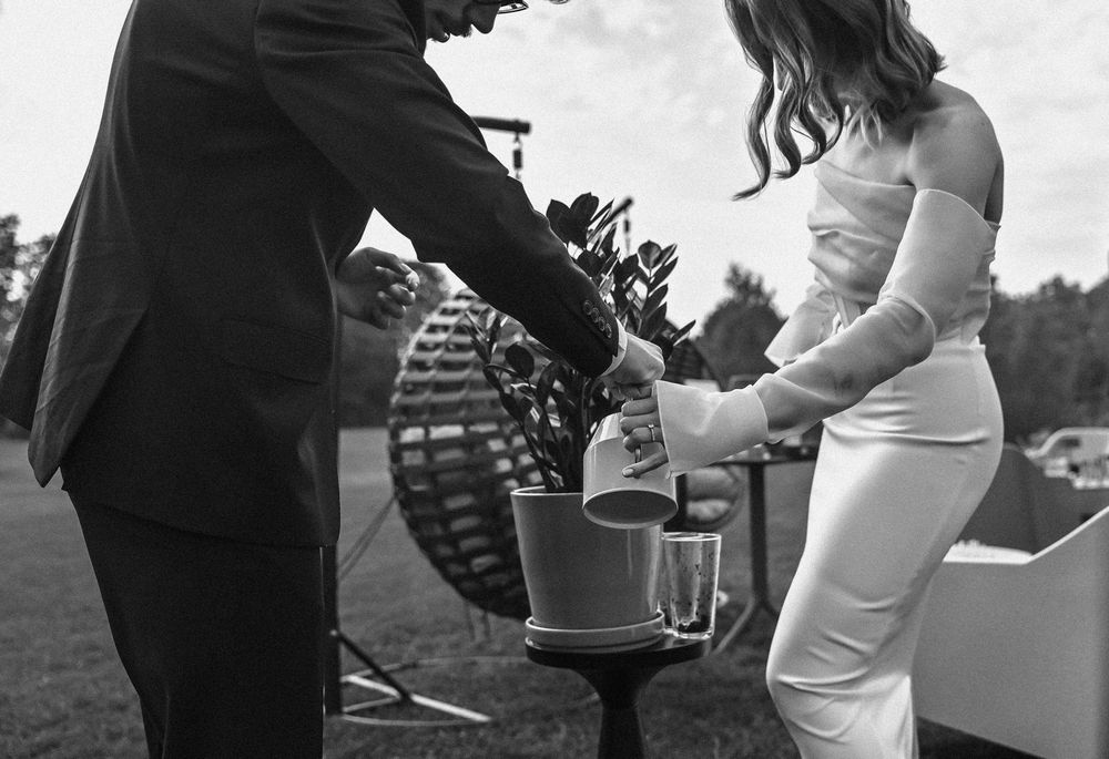 Couple in formal attire dances closely together during a romantic outdoor reception by a rustic wooden barn.