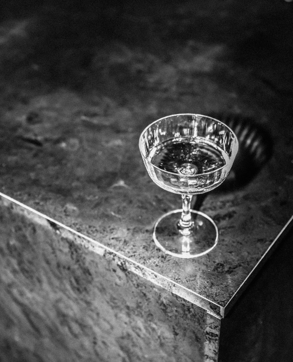 Classic champagne coupe glass on textured stone surface in black and white.
