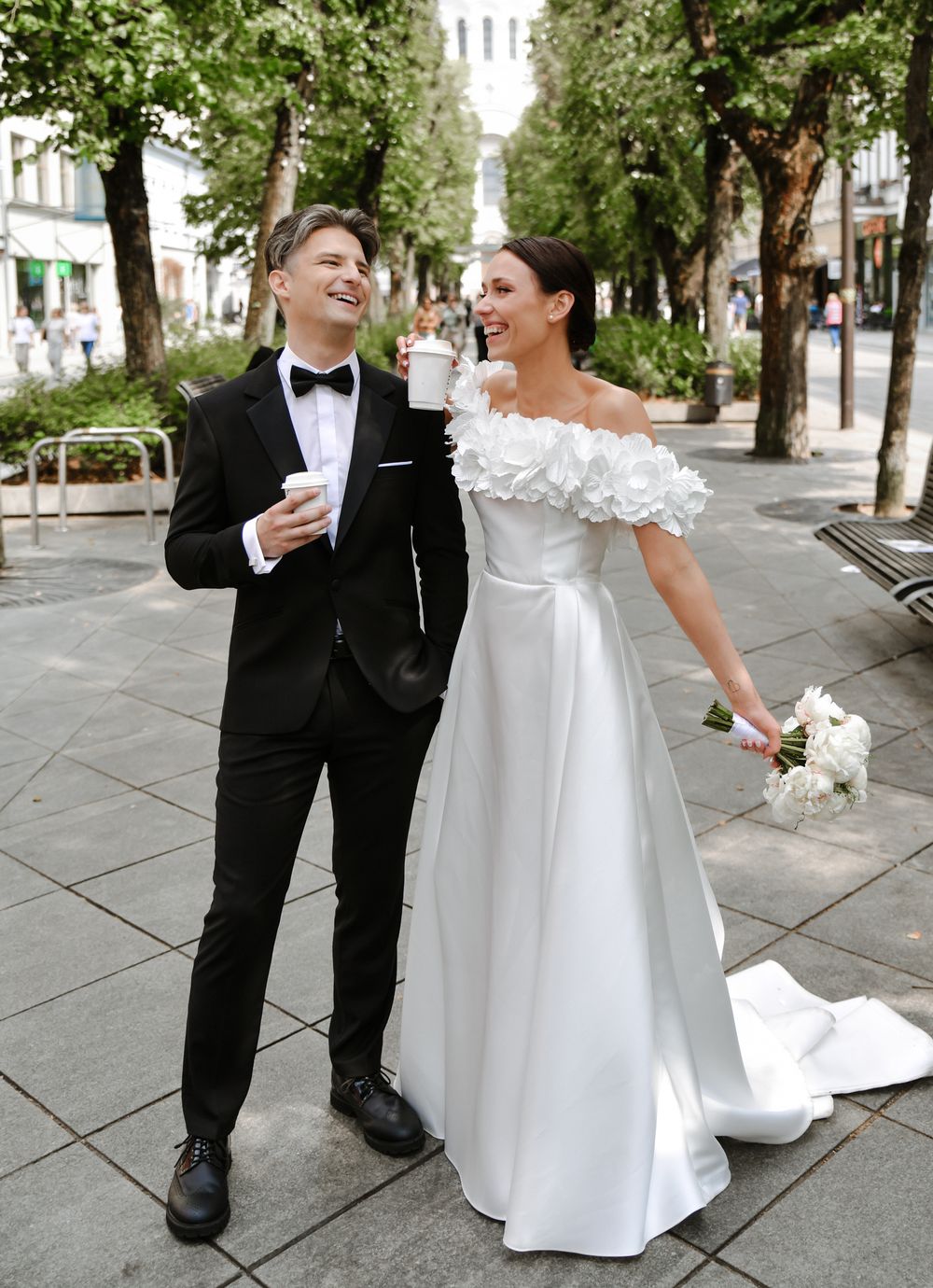 A cheerful newlywed couple walking along a tree-lined city street.