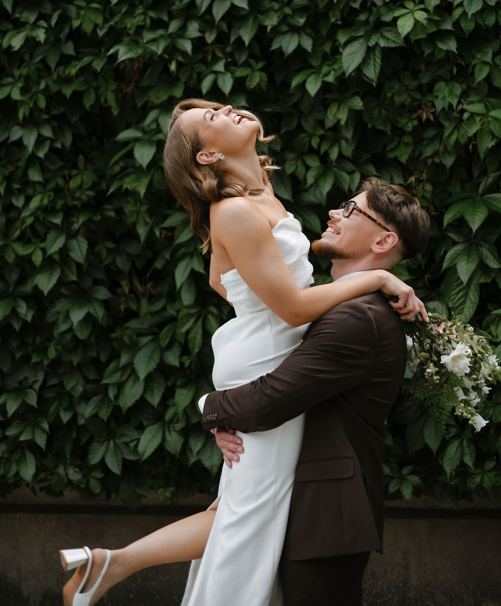 A romantic couple shares intimate moments against a lush green ivy wall backdrop during their wedding photoshoot.