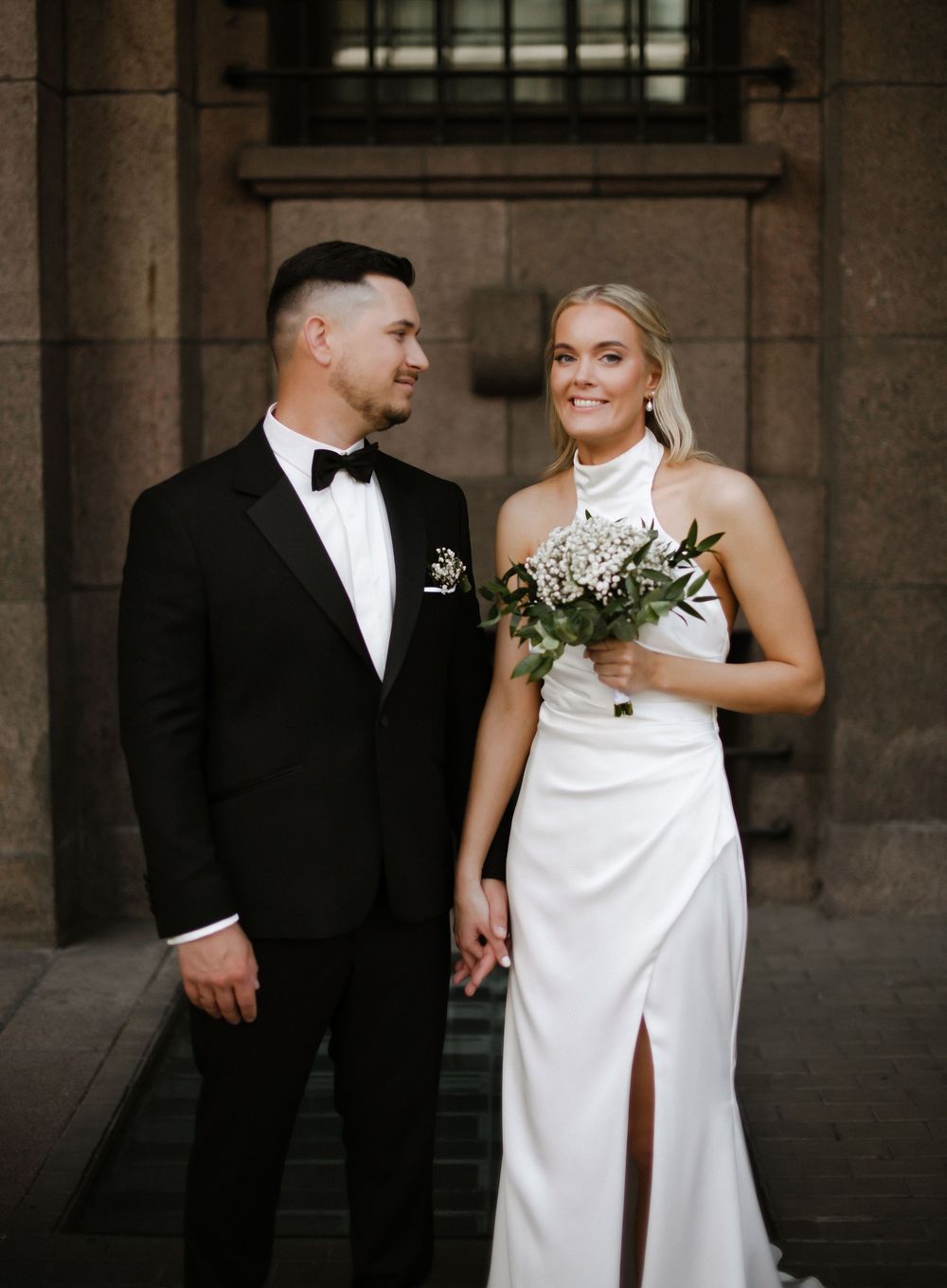 A bride and groom share intimate moments in an elegant stone archway setting during their wedding photoshoot.