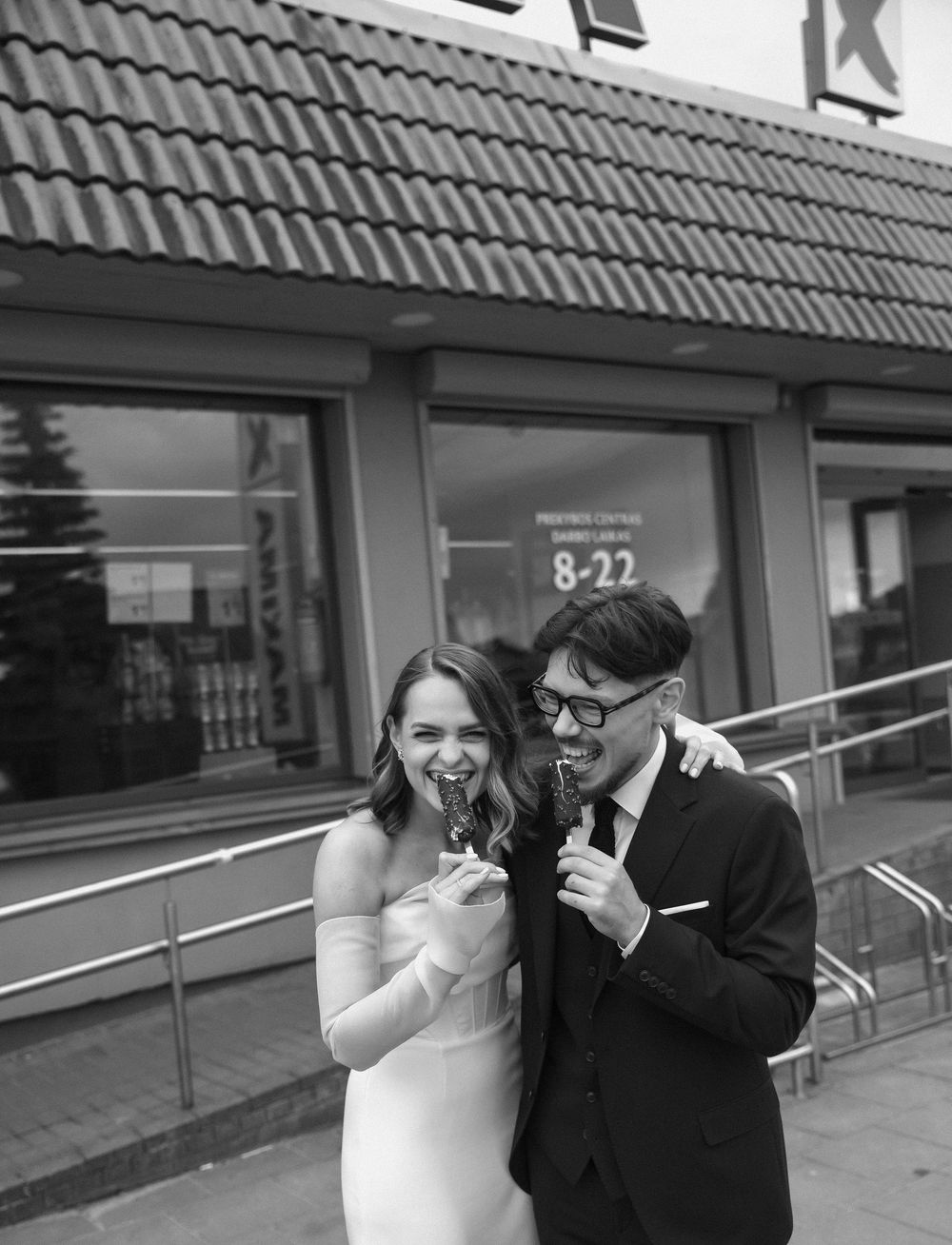 A couple in wedding attire laughs together in a playful sequence of black and white photographs outside a building.