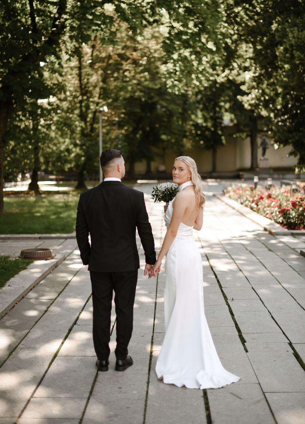 A bride and groom walk away together on a stone path in a garden setting during their wedding day.