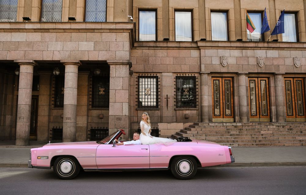 A pink vintage convertible Cadillac parked in front of a historic stone building with columns.