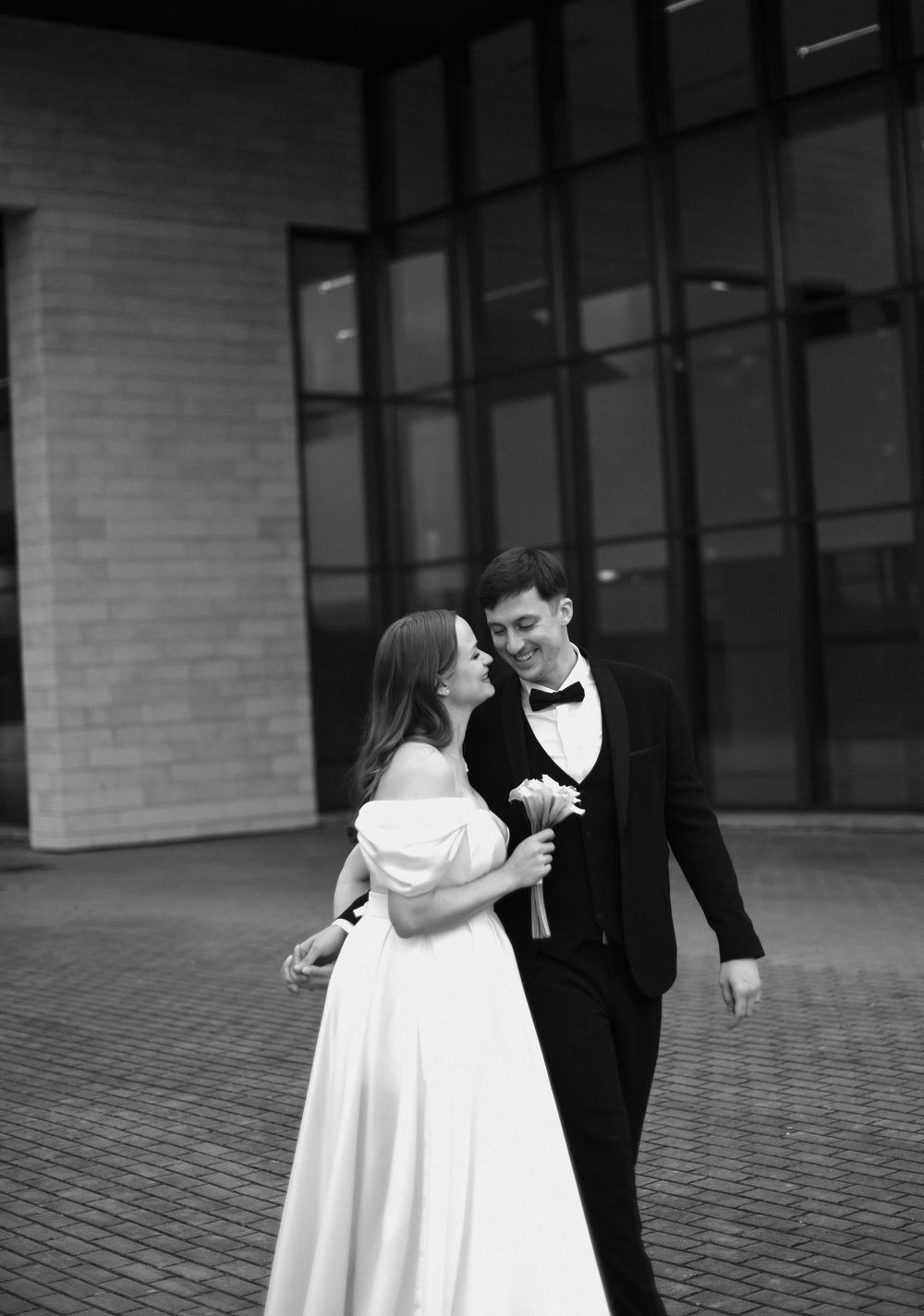 Black and white photo of a couple sharing an intimate dance moment on a paved walkway.