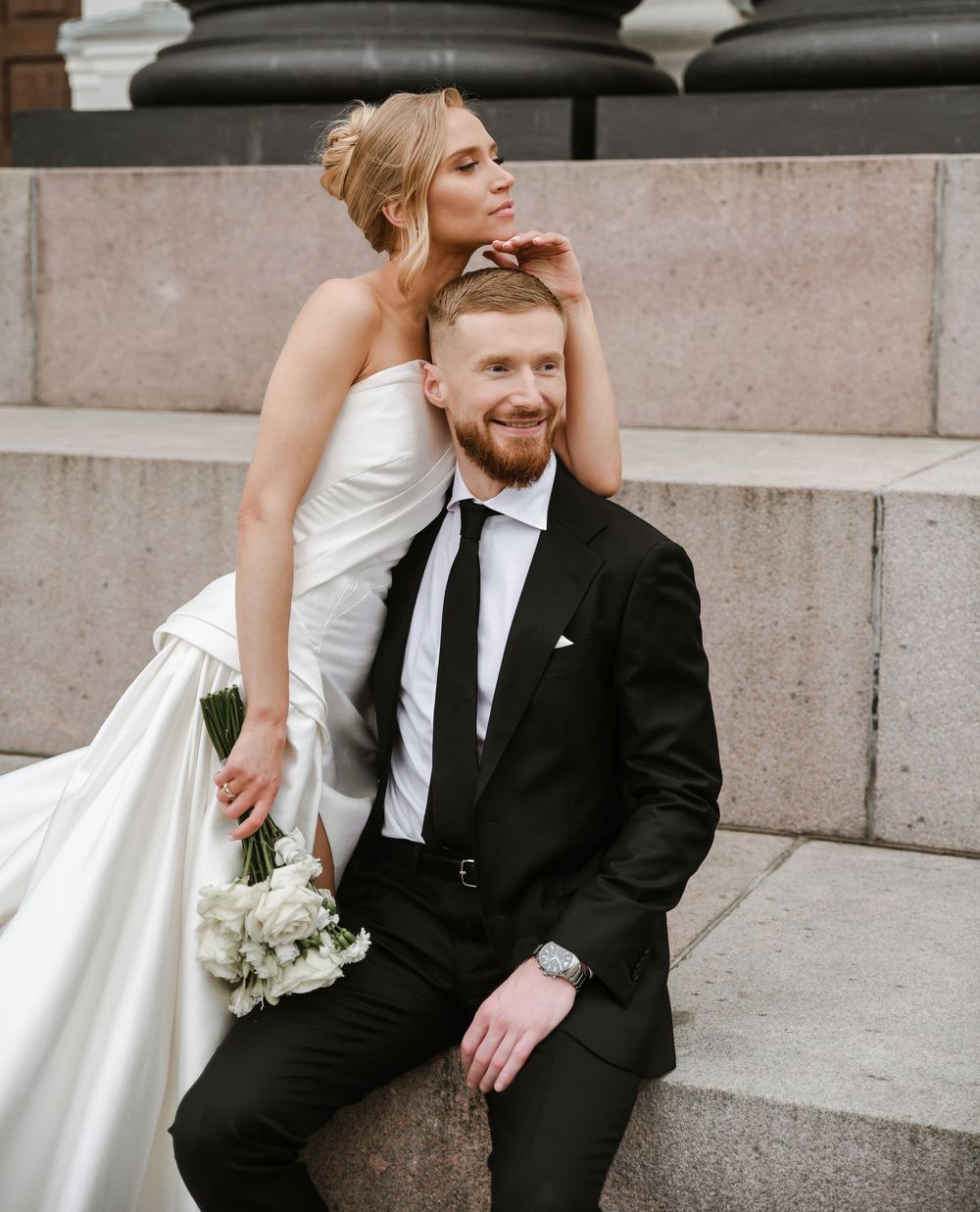 A bride and groom share a tender moment sitting on stone steps during their wedding photoshoot.