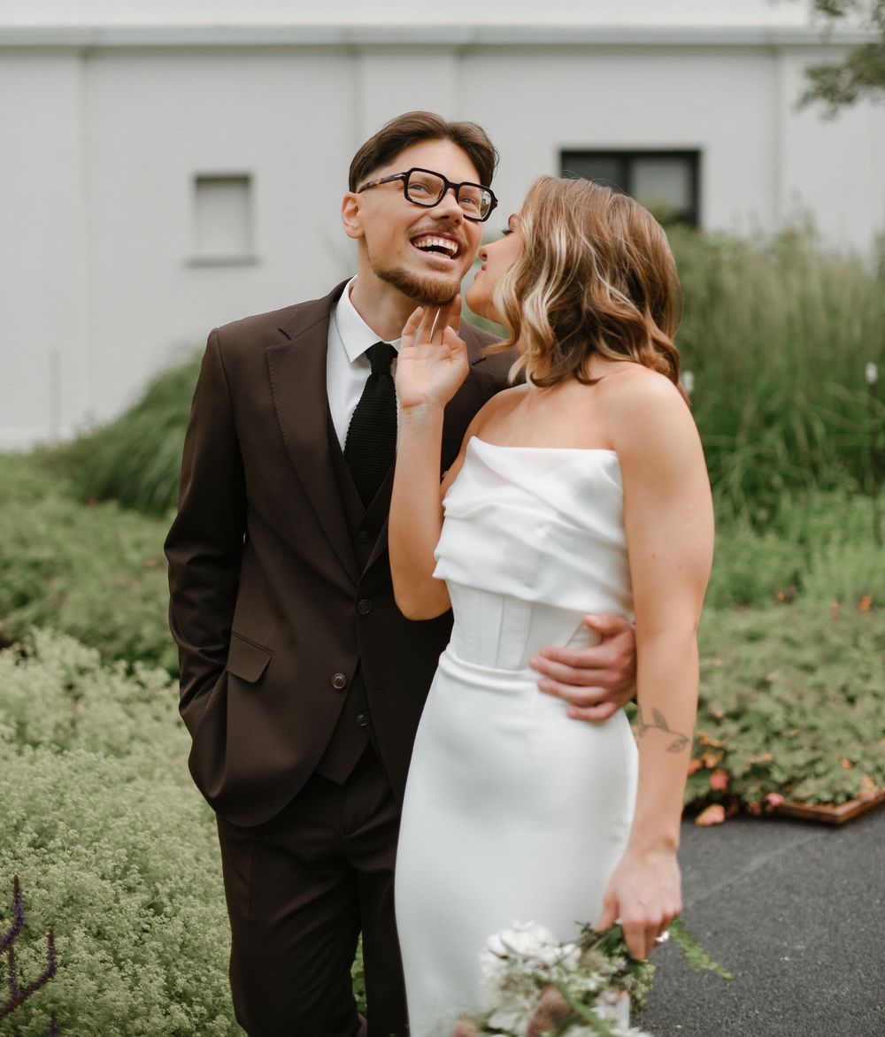 A couple shares an intimate moment in a garden setting, with the bride wearing a white dress and groom in dark suit.