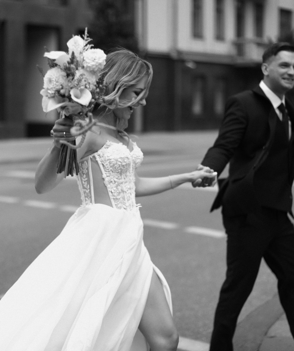 A wedding couple shares a playful moment in black and white as the bride's dress flows in the wind.