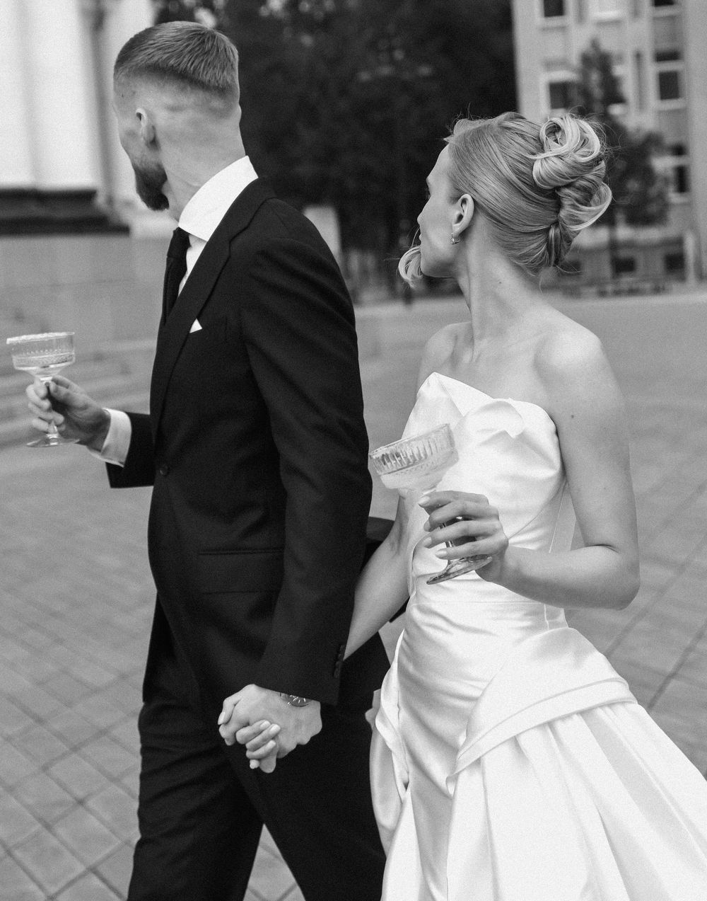 A couple in wedding attire toasts with champagne glasses on an outdoor patio.