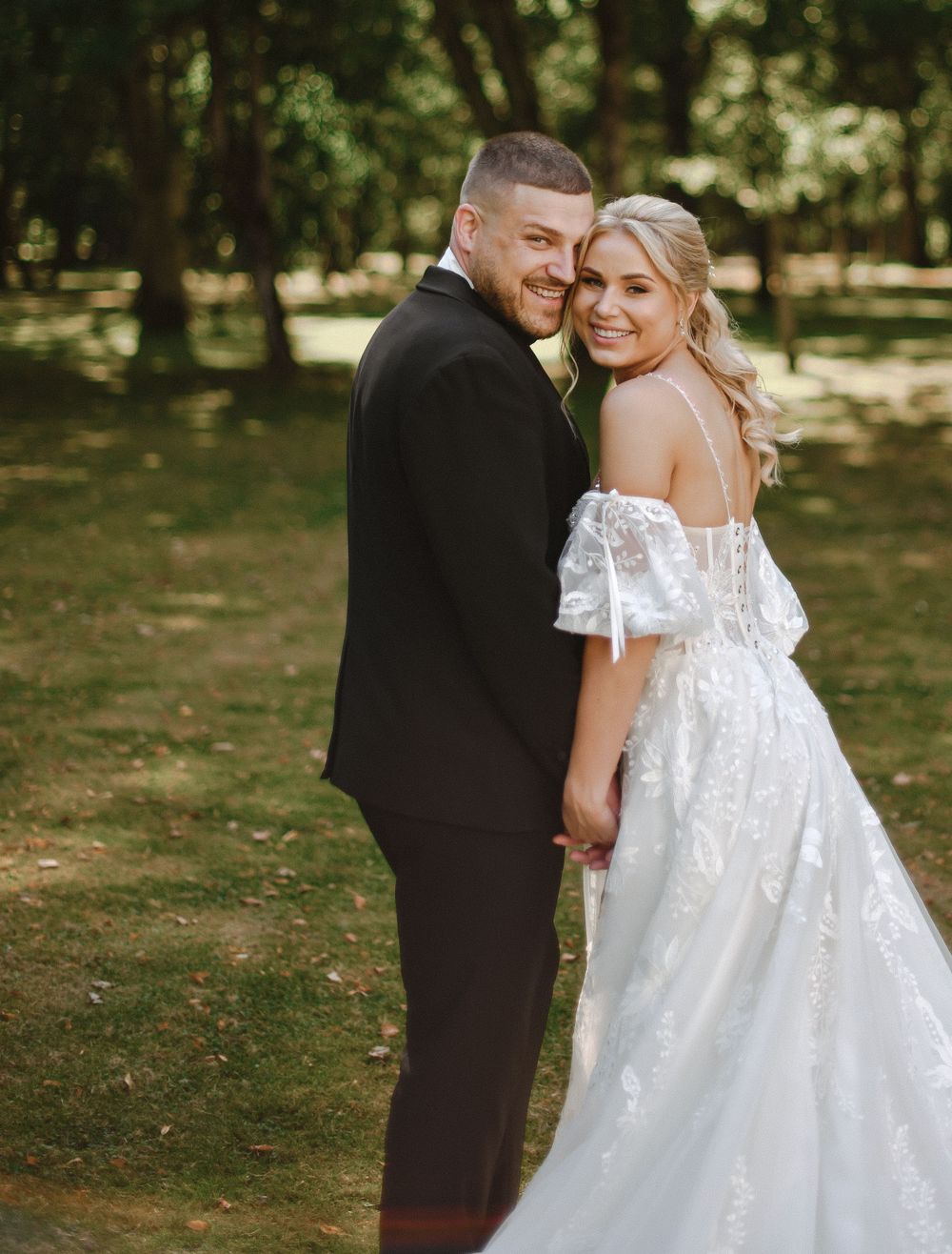 Romantic outdoor wedding portrait with couple embracing under tree canopy.