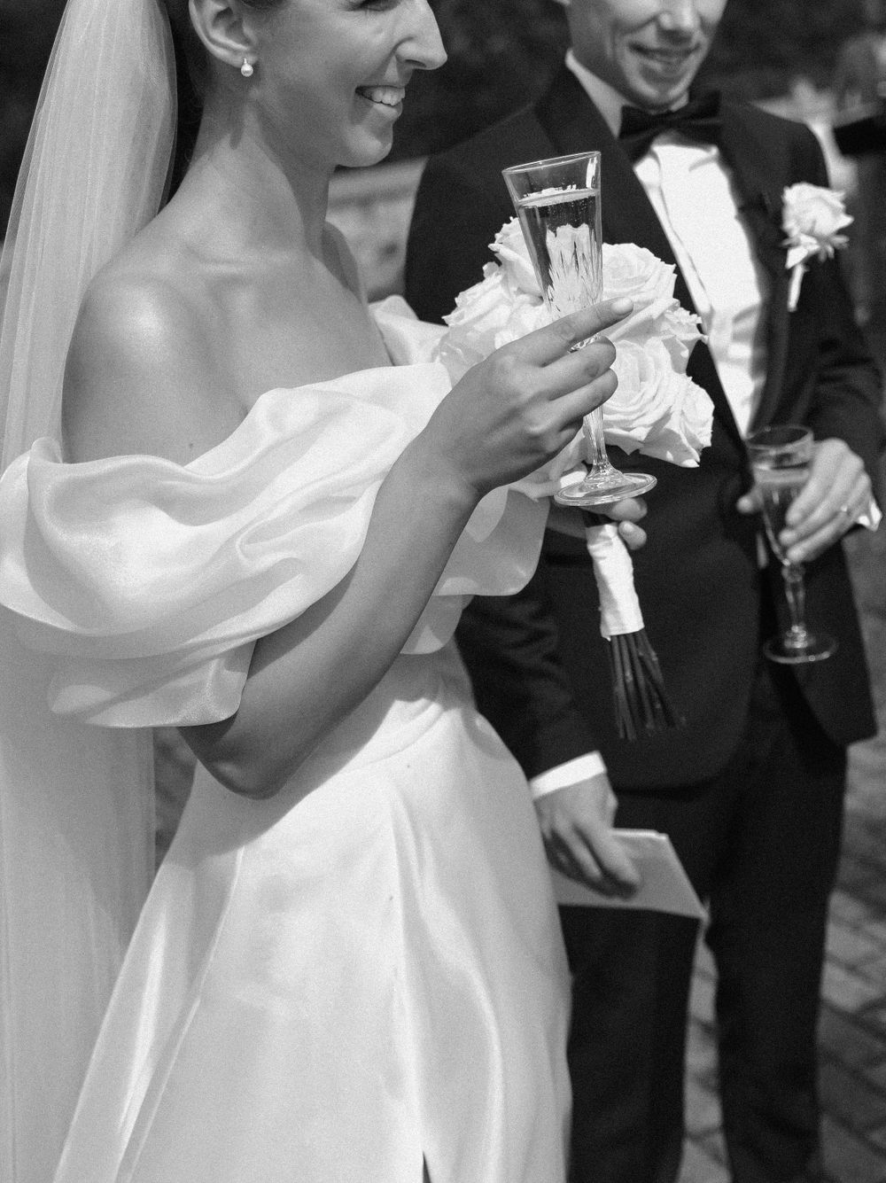 A black and white photo captures newlyweds sharing champagne after their ceremony.