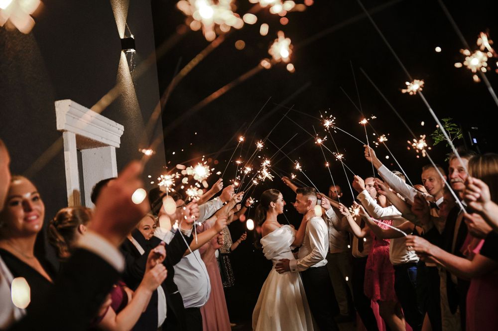 Wedding guests hold sparklers creating magical tunnel of light during evening celebration.