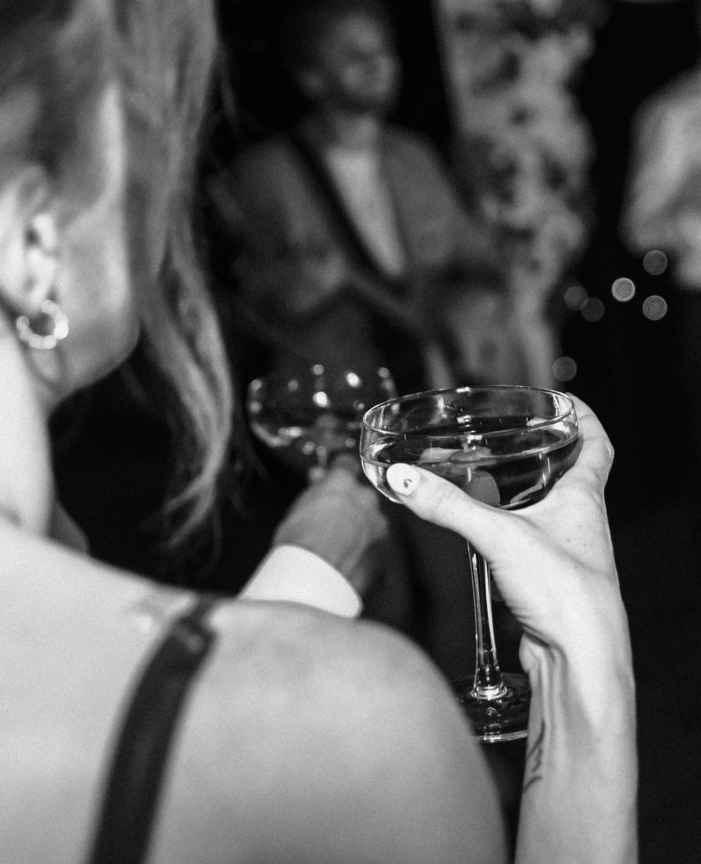Black and white close-up of champagne glasses during wedding toast.