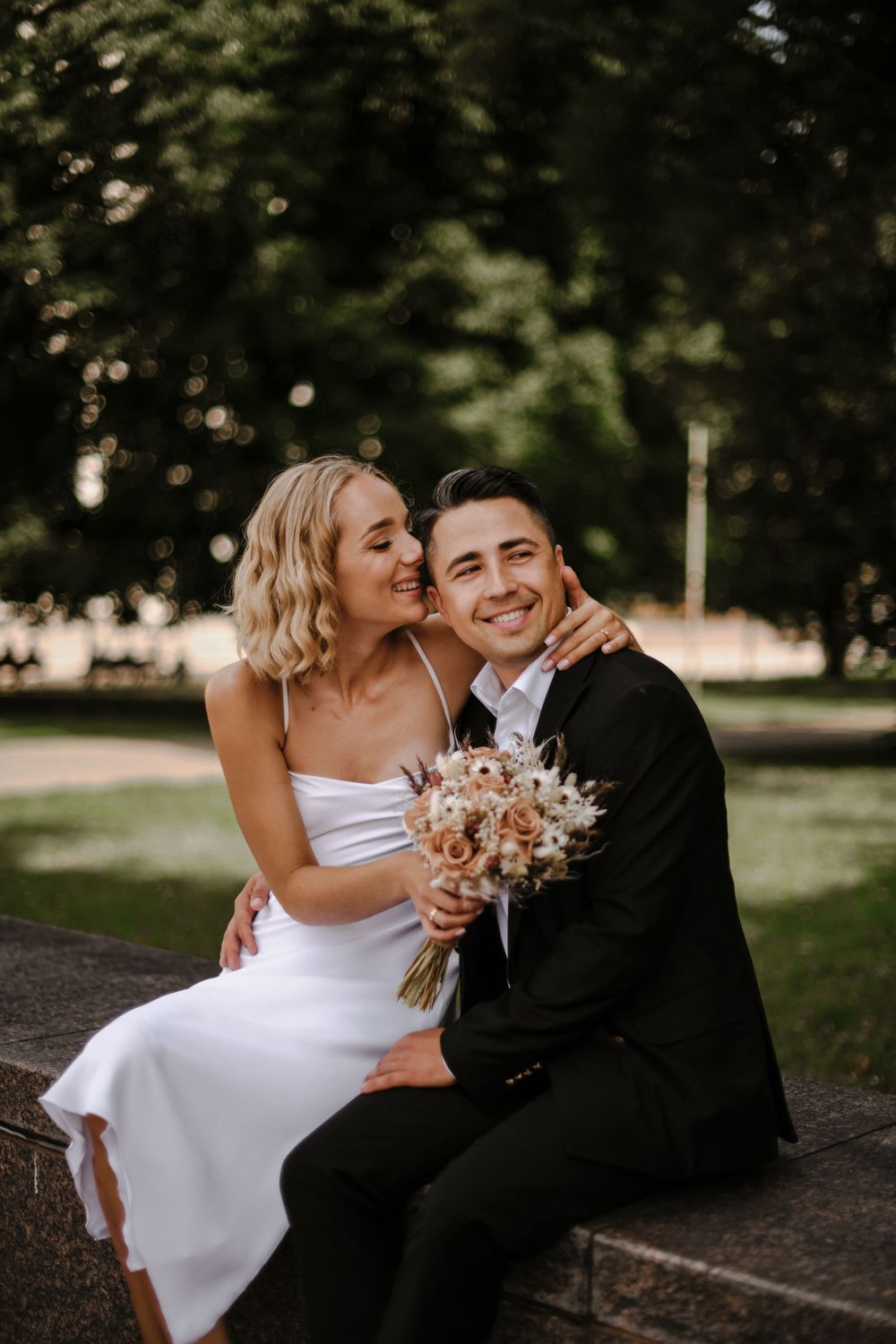 Intimate wedding portraits captured on park bench with natural lighting and floral bouquet.