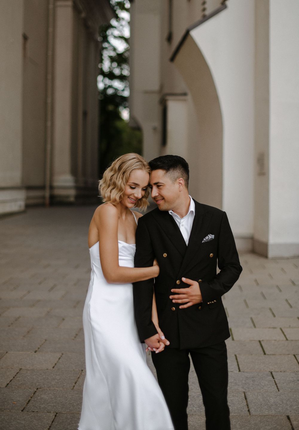 Elegant wedding photos under white columned architecture showing tender moments.
