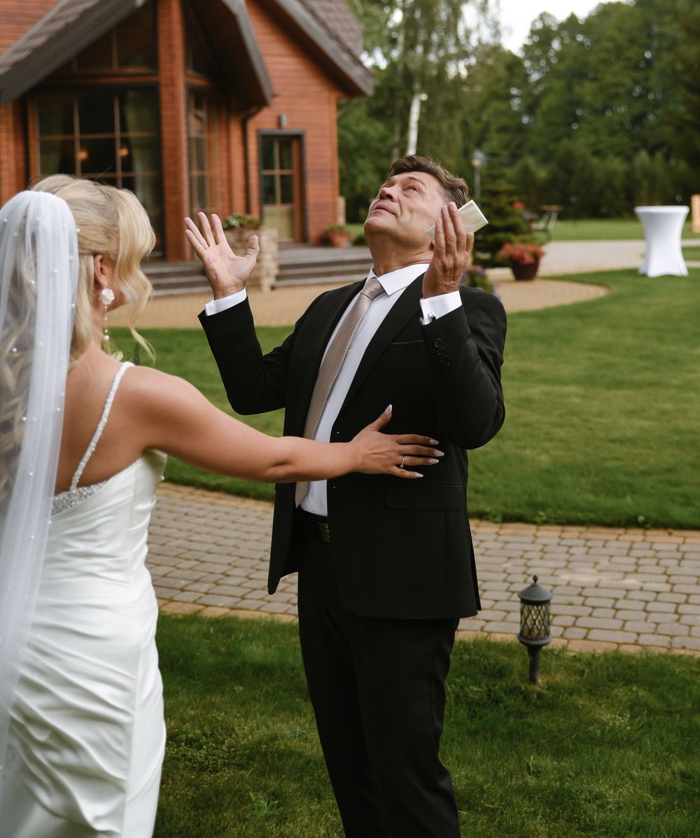 A bride and groom share a candid moment on their wedding day outside a rustic wooden building on a landscaped lawn.