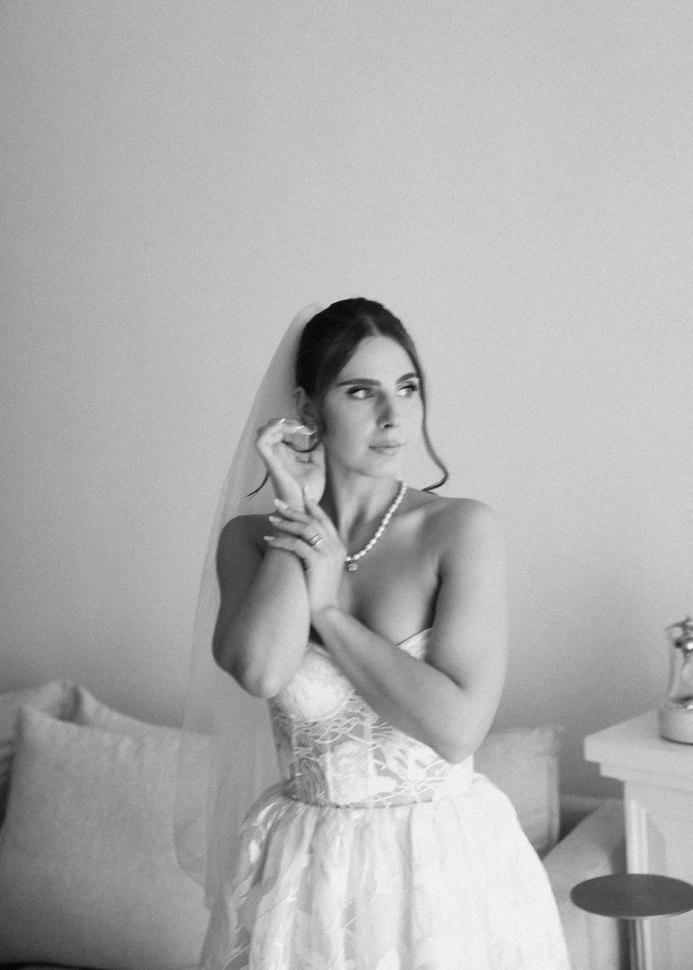 A bride in a strapless white wedding gown and veil poses elegantly in black and white photography.