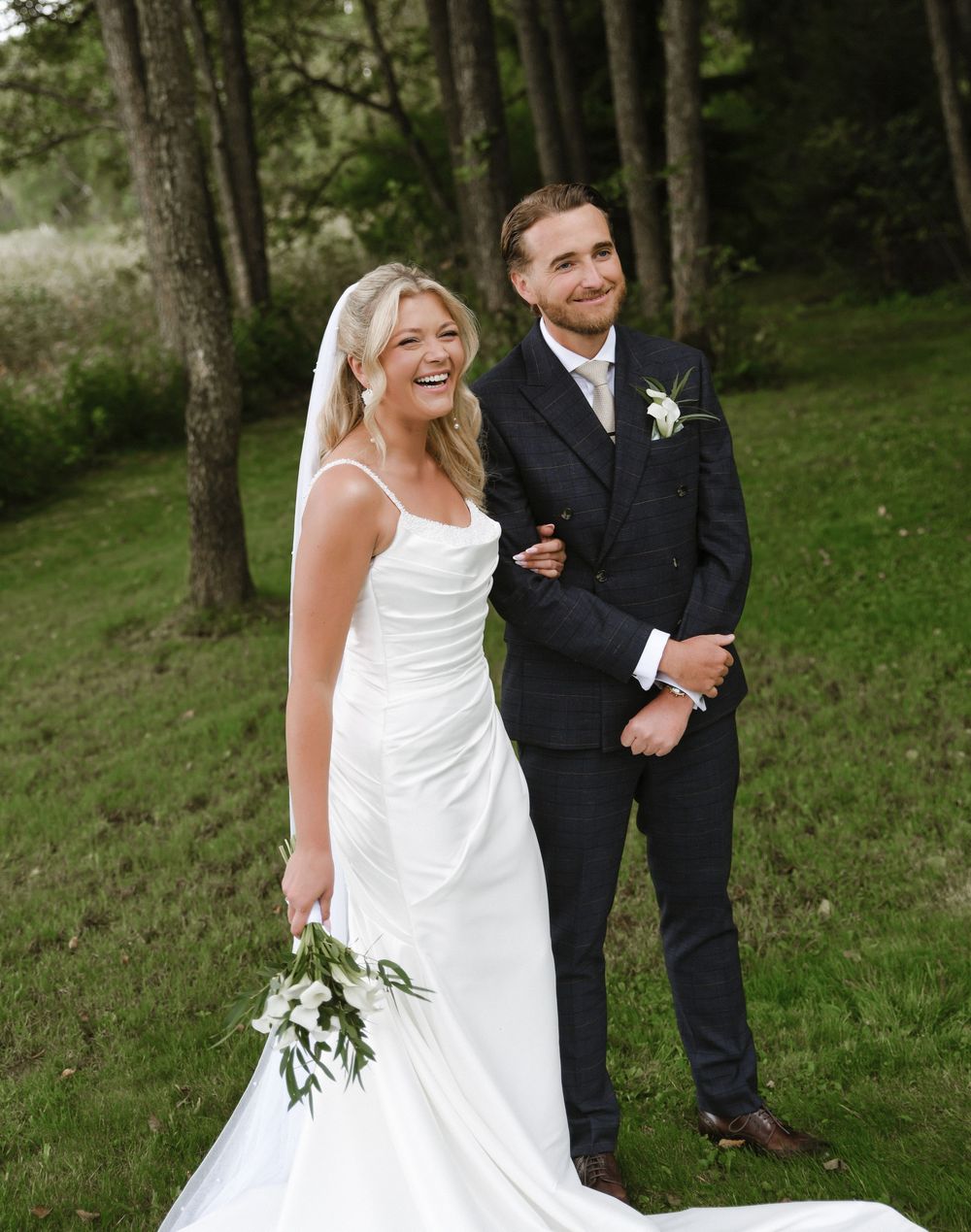 A couple shares joyful moments in a wooded outdoor setting during their wedding photoshoot.