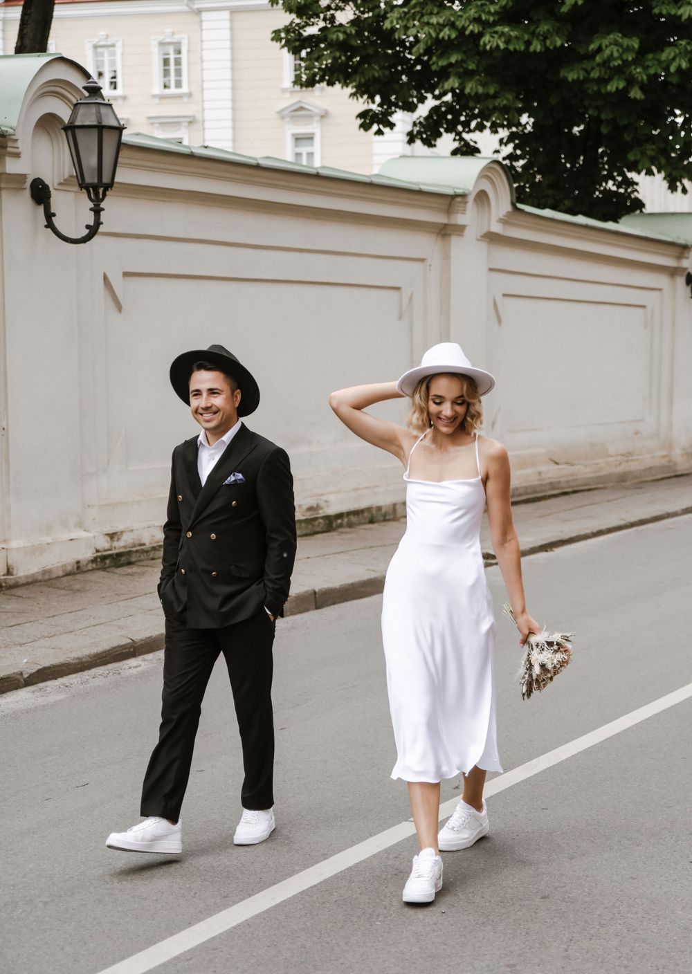 Modern casual wedding couple in black and white outfits walking down city street.
