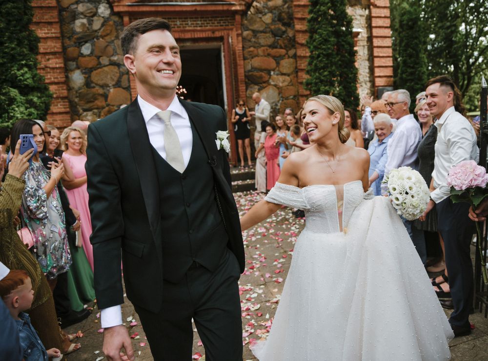 Joyful wedding celebration outside stone building with guests in formal attire.
