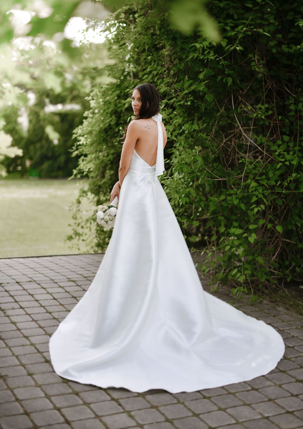 Full-length view of elegant backless wedding gown with flowing train in garden setting.