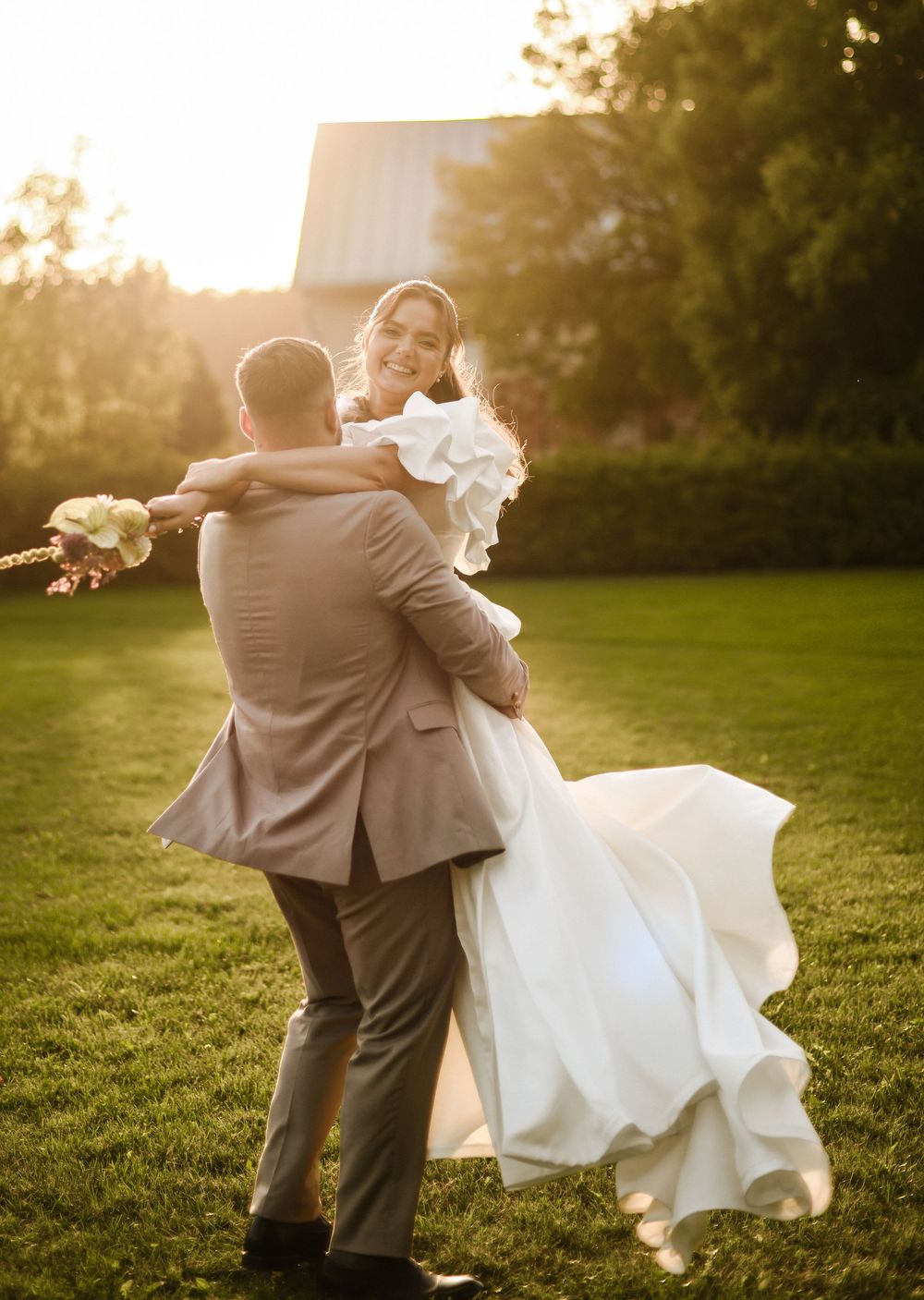 A romantic couple dances together on a grassy lawn during golden hour sunset.