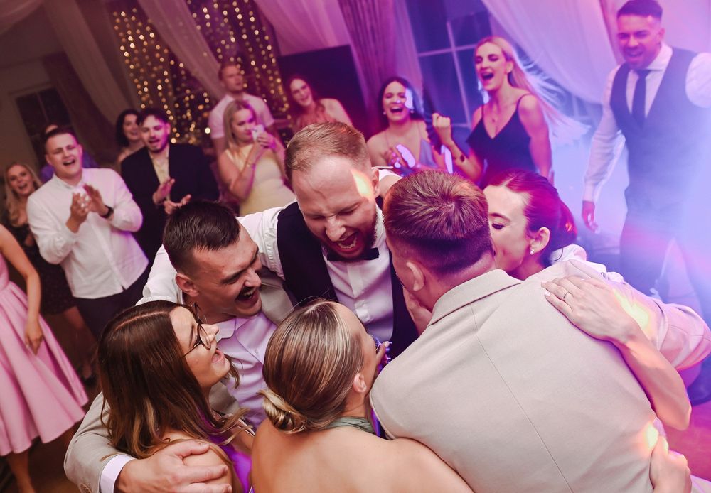 Wedding guests celebrating and dancing together at a reception with purple lighting and festive atmosphere.