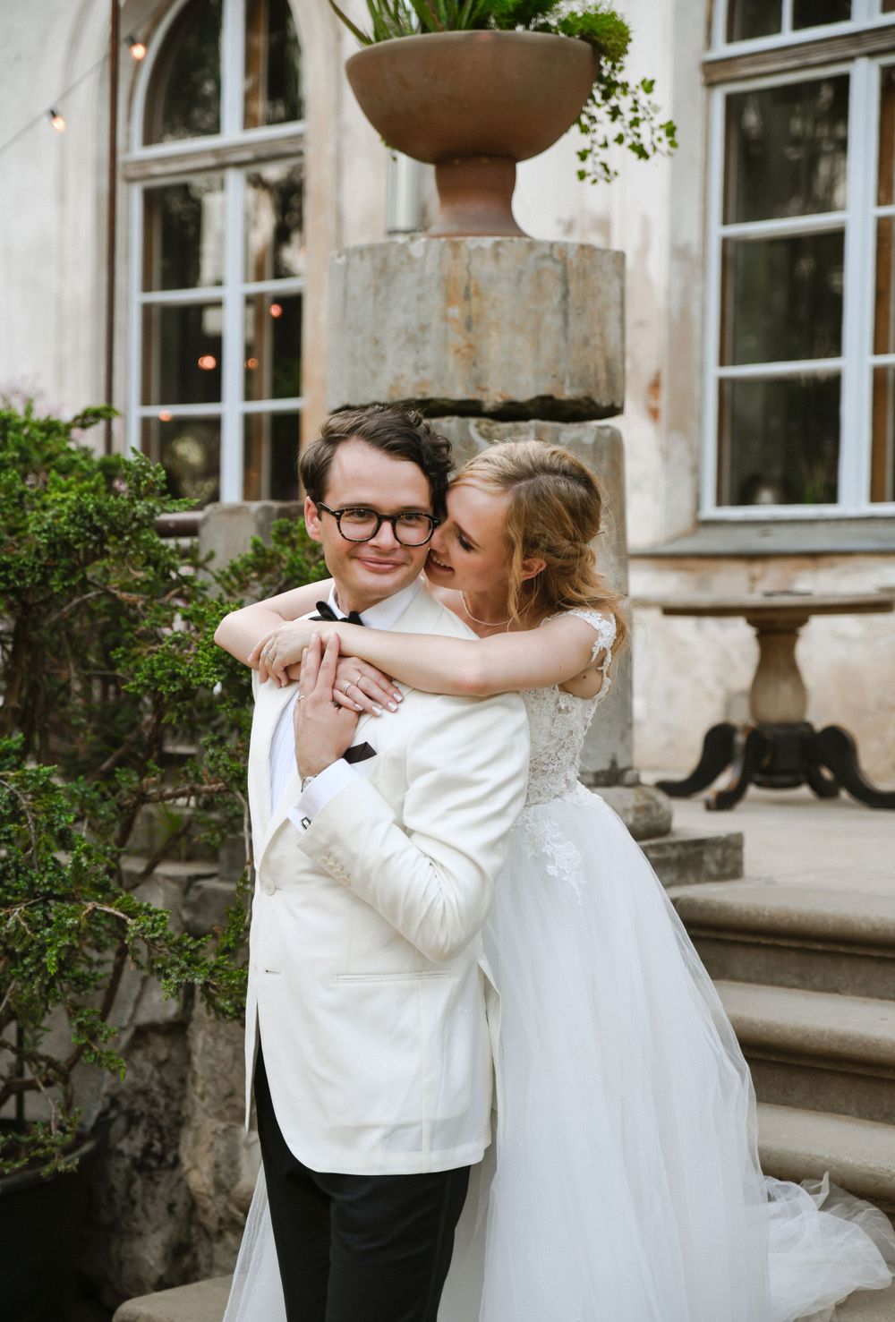 Romantic moment captured in front of historic building with decorative garden urn and windows.