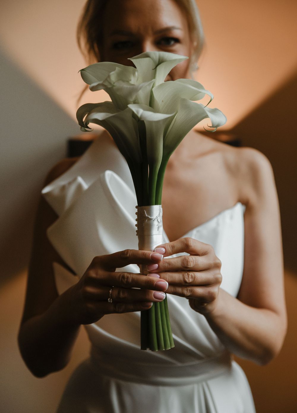 Close-up of white calla lily bouquet held by person in wedding dress.