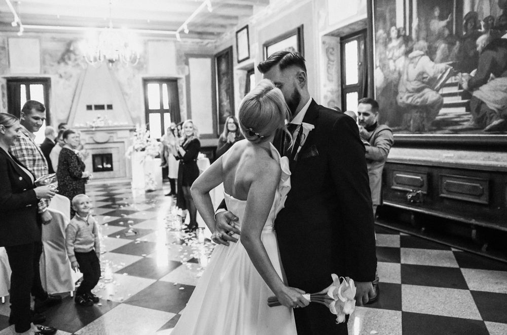 Black and white photo of wedding couple dancing in a grand hall with checkerboard floor.