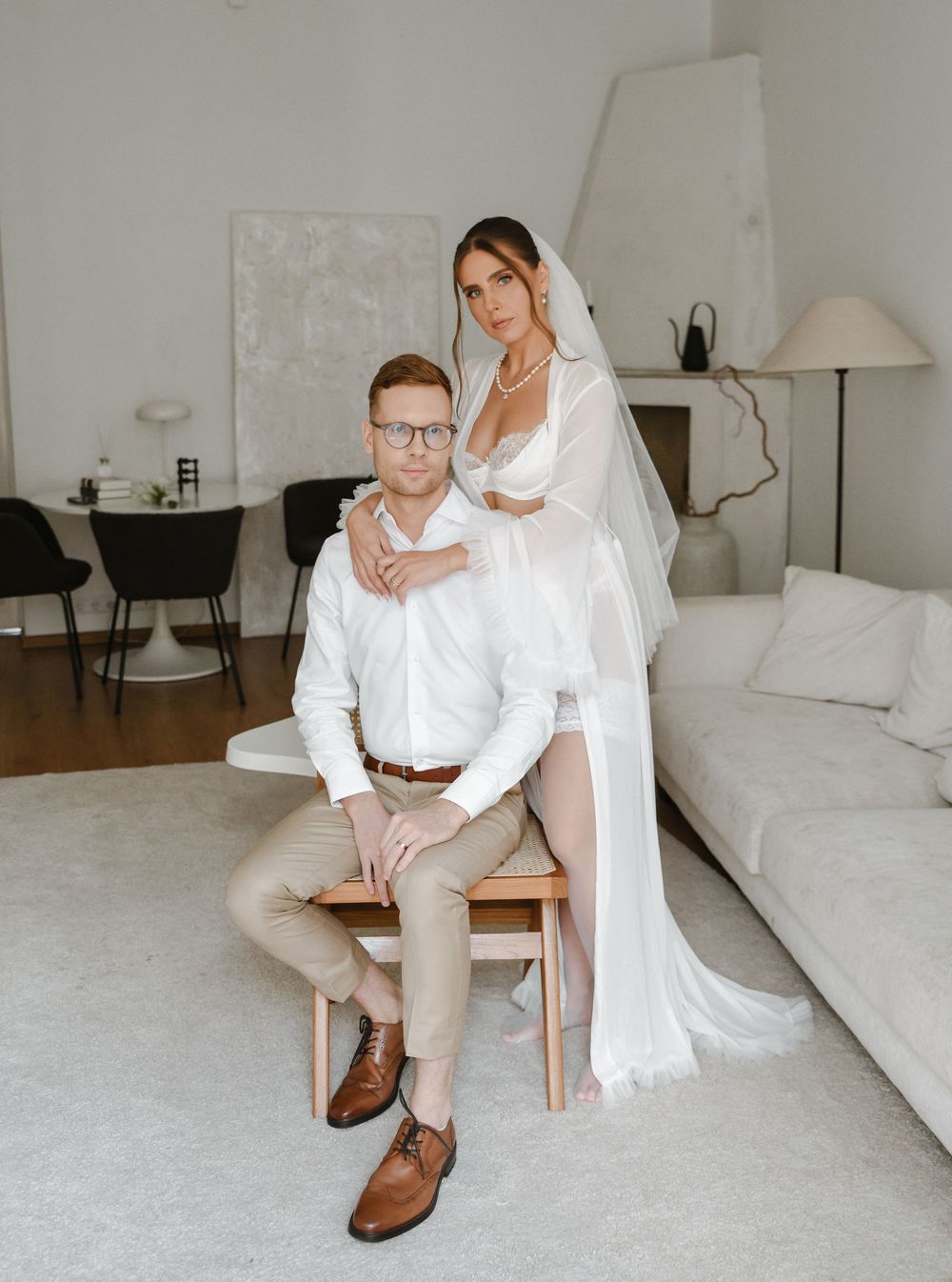 Couple shares an intimate moment in white outfits during their engagement or wedding photoshoot in a bright room.