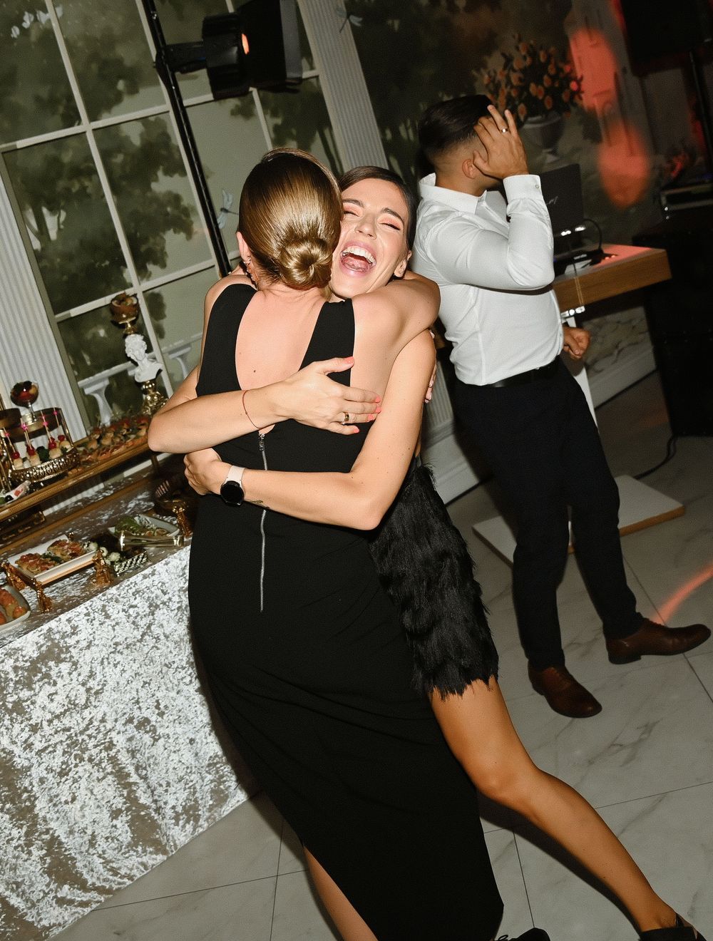 Two people dancing together in black outfits at a party with a white tablecloth visible in the background.