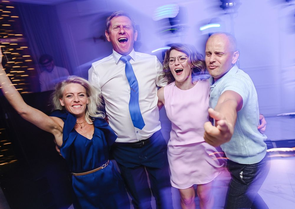 People dancing and celebrating together at a party with blue lighting and energetic atmosphere.