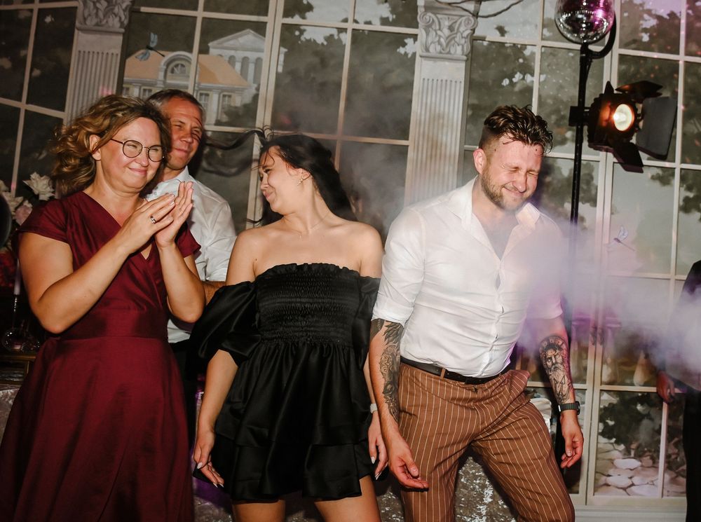 Wedding guests dance together on a dance floor during a reception celebration with colorful lighting.