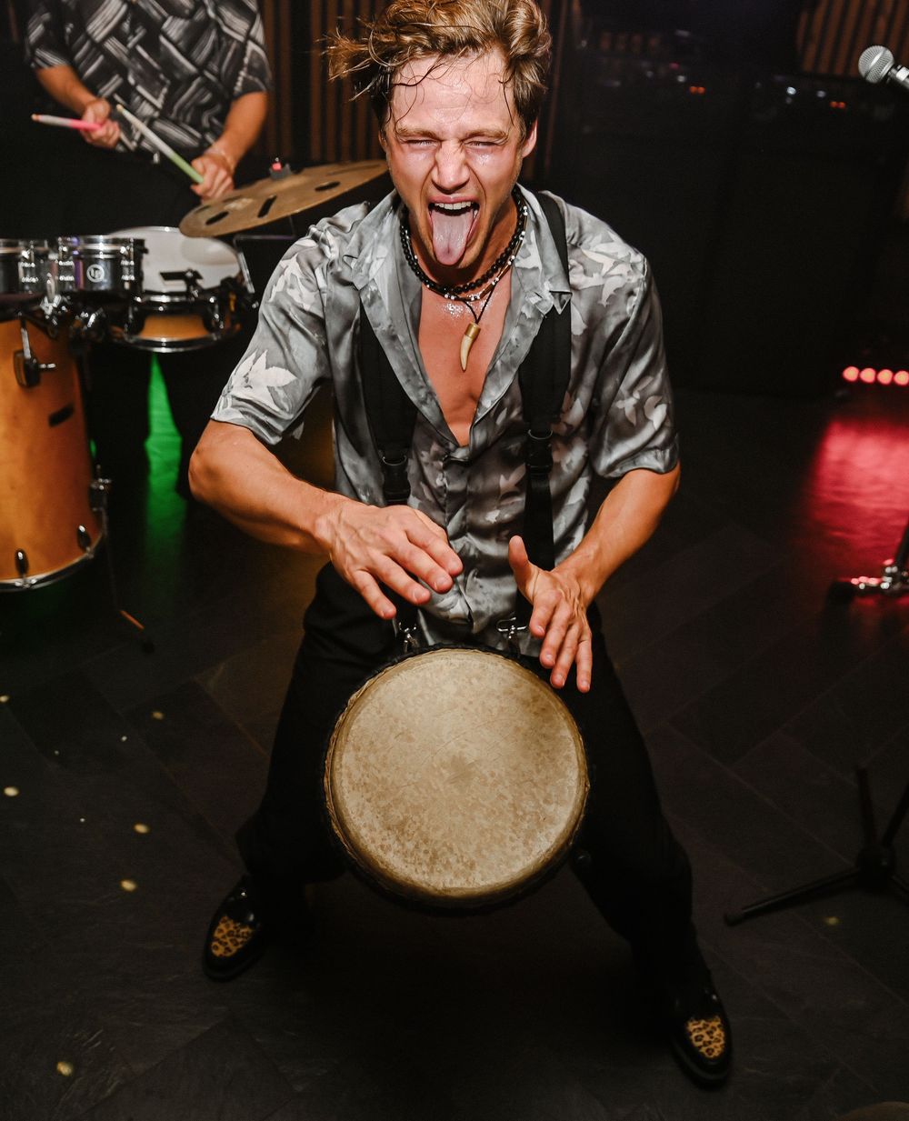 A musician plays an energetic performance with a drum on stage in a dimly lit venue.