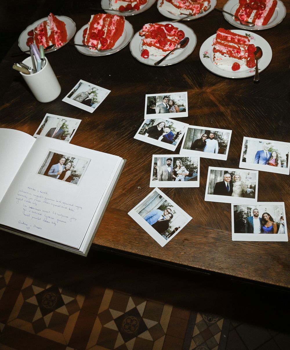 A collection of polaroid photos spread across a wooden table with a decorative patterned floor visible.