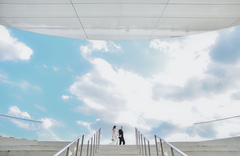 Silhouette of person walking across white bridge against bright blue sky with fluffy clouds.