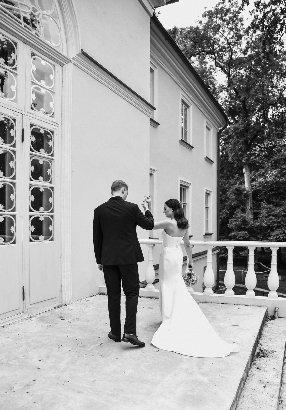Wedding couple poses for romantic black and white photos along an ornate white balcony.