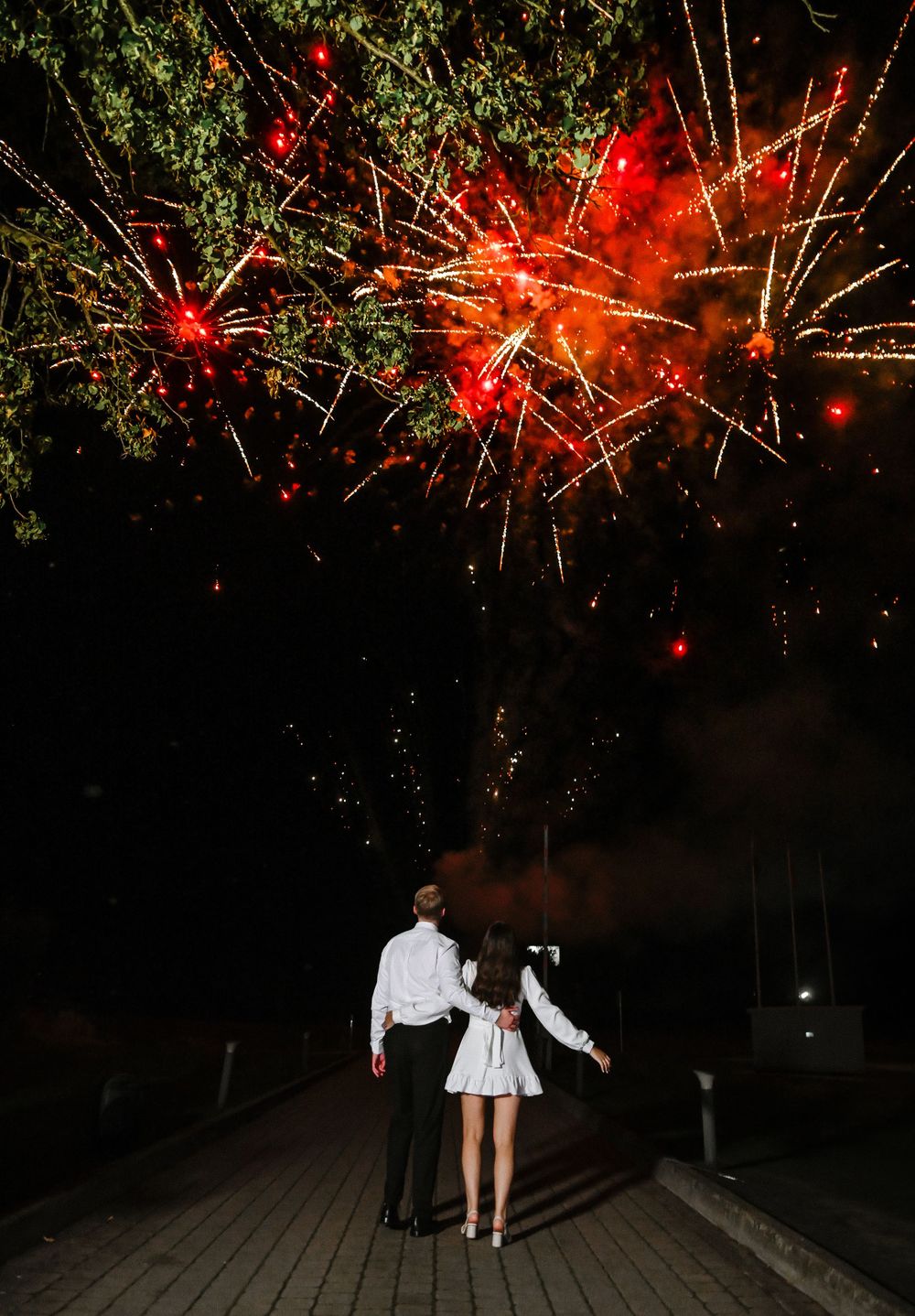 A couple watches red fireworks display during their wedding celebration.