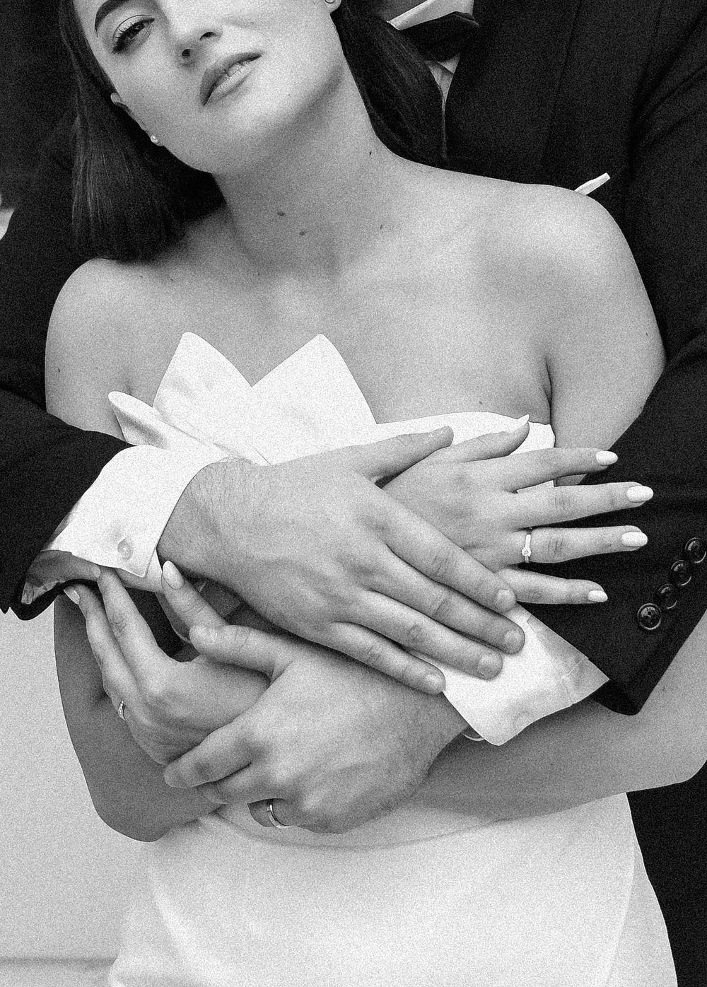Detail shots of hands embracing in black and white against a white wedding dress.