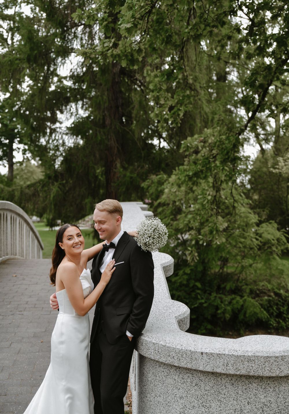 Romantic wedding portraits on a white stone balcony surrounded by lush greenery.