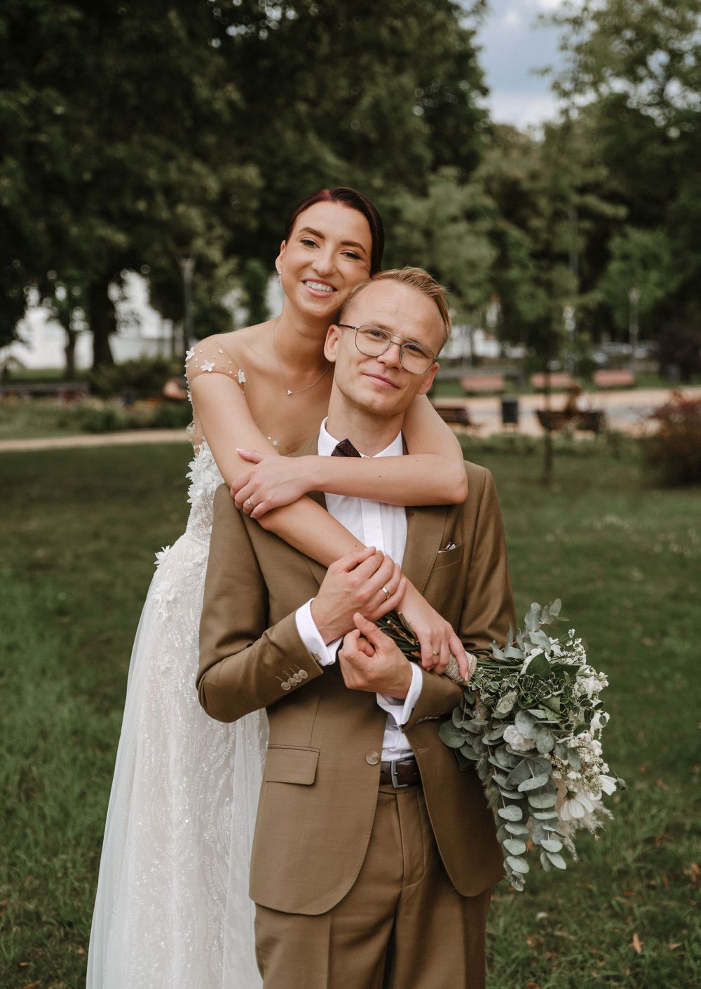 A romantic portrait of a couple embracing outdoors on their wedding day with a natural greenery backdrop.