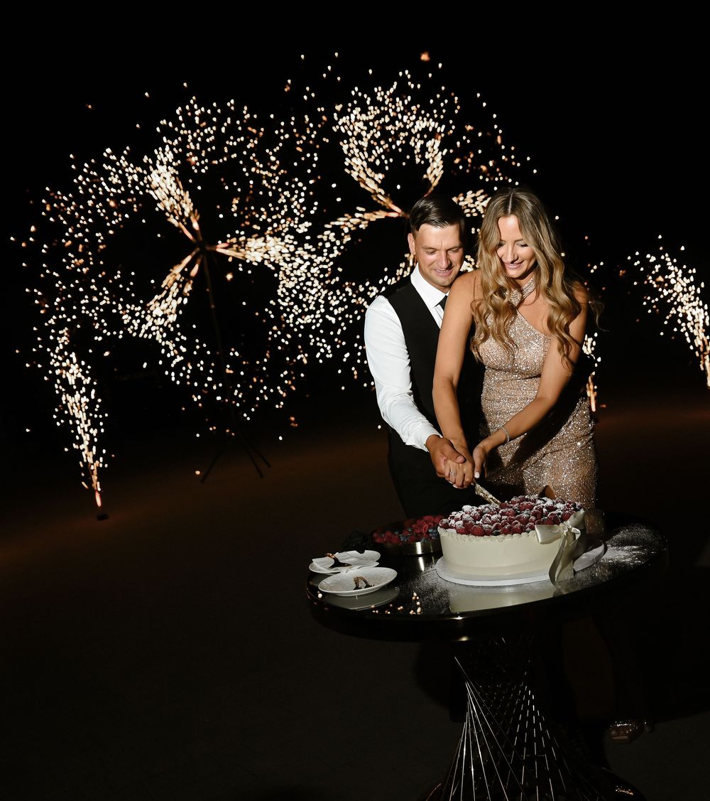 Sparkling fireworks illuminate a romantic couple dancing at their wedding reception on a dark dance floor.