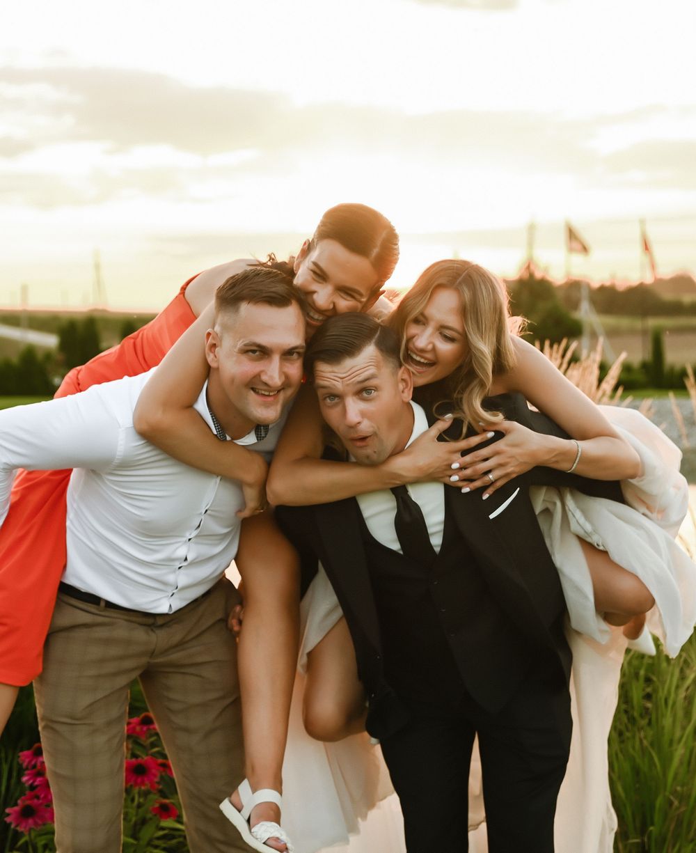 A joyful group embraces and laughs together outdoors during a wedding celebration at sunset.