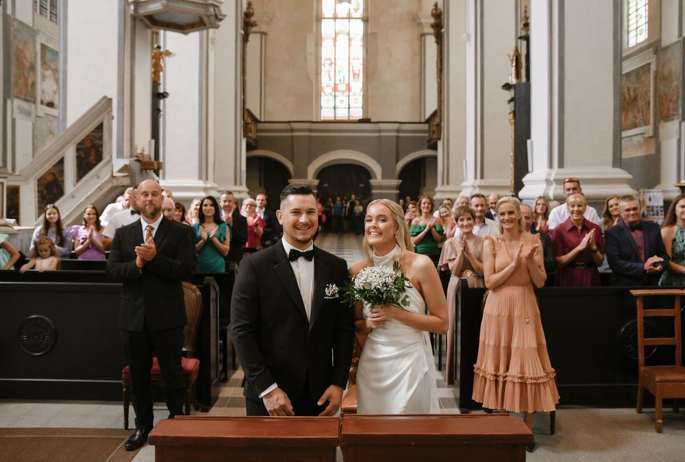 Wedding ceremony takes place in a historic church with guests applauding from wooden pews.
