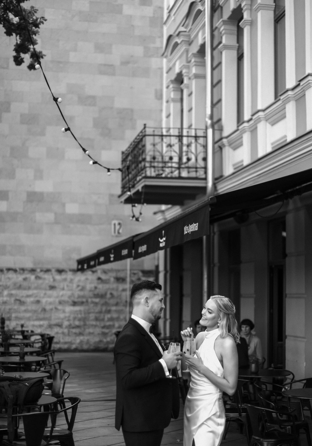 Romantic black and white wedding photos showing couple embracing on a covered brick patio with classic architecture.