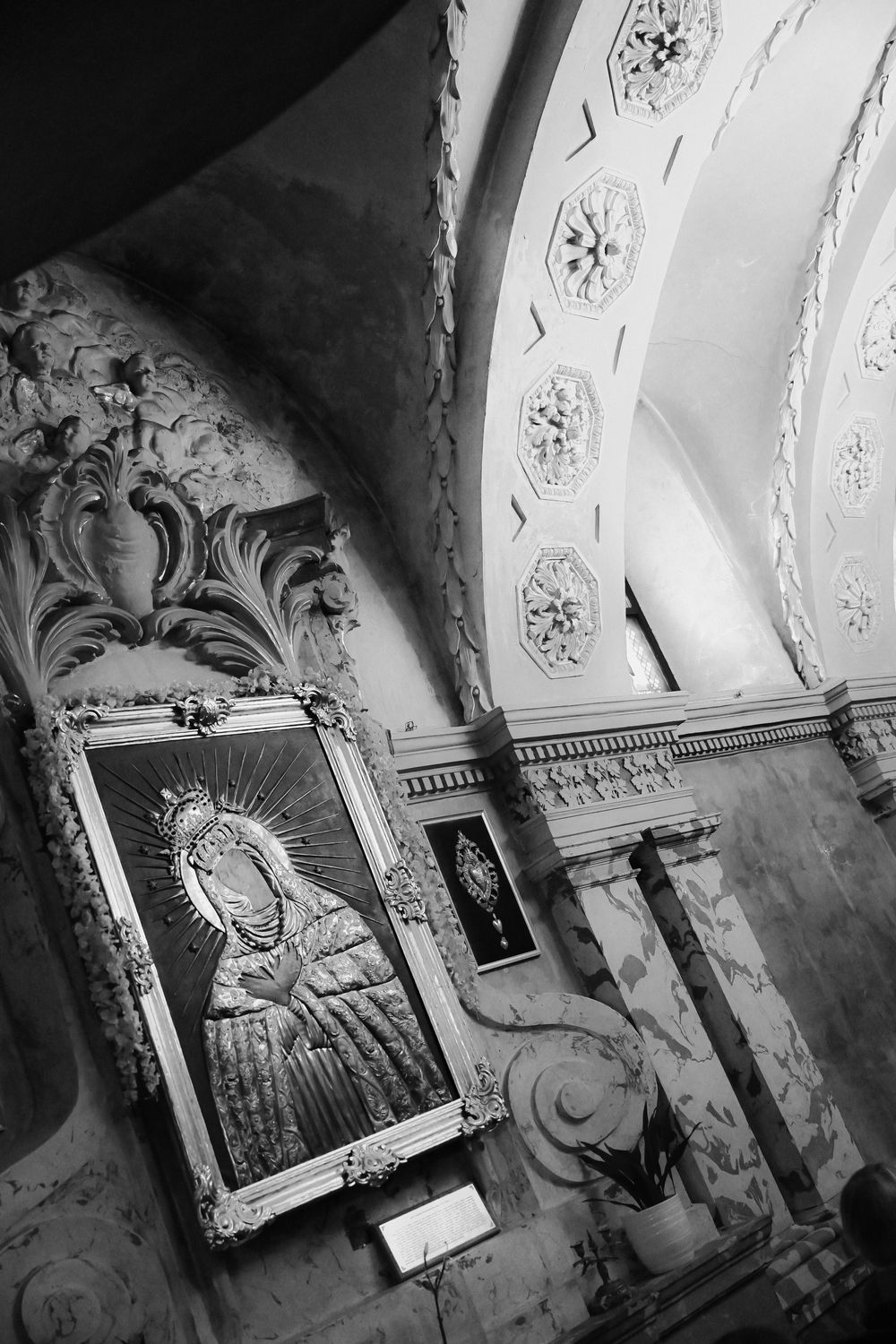 Black and white photo of ornate church interior with Virgin Mary icon in gilded frame and decorative baroque ceiling.