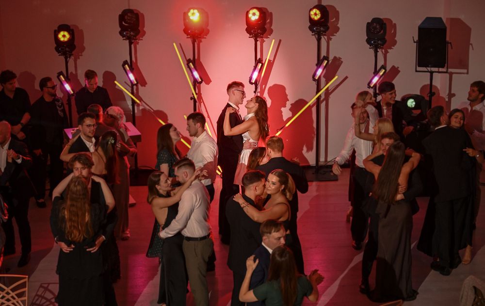 Couples dancing at a formal event with colorful stage lighting and light-up props in a festive ballroom setting.
