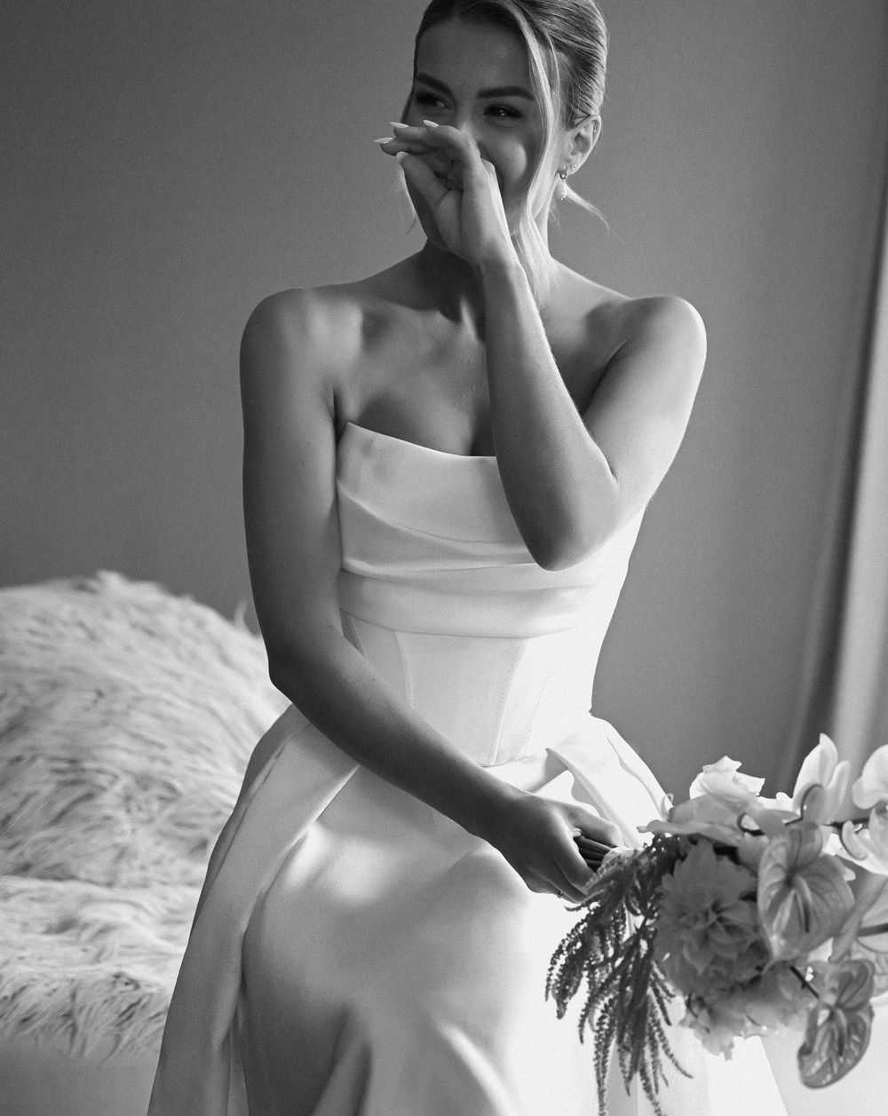 Black and white photo of an emotional bride in a strapless gown holding a bouquet, wiping a tear on her wedding day.