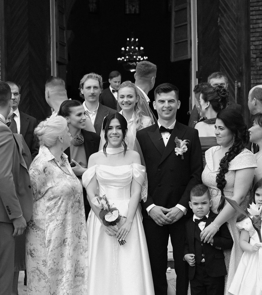 Black and white wedding photo of bride and groom posing with family and guests outside a church.
